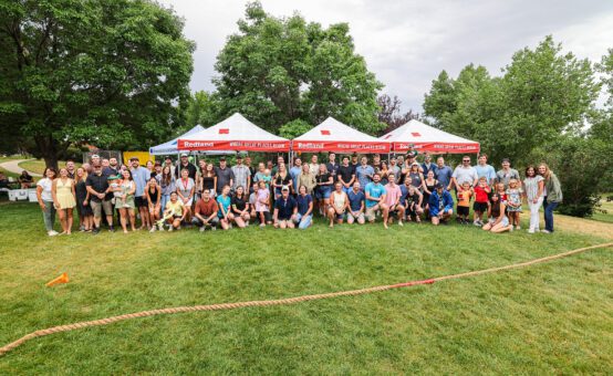 Large group photo of people standing in a park in front of three red and white tents.